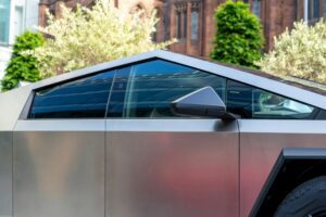 Tesla Cybertruck med futuristisk design og skinnende metal finish, parkeret foran en bygning omgivet af grønne træer
