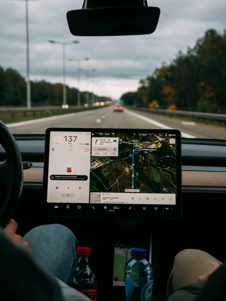 Indvendig visning af en Tesla med navigationssystemet synligt på skærmen, mens de kører på motorvejen en overskyet dag