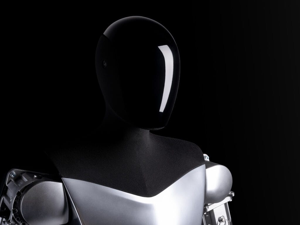 Tesla humanoid robot med sort glat ansigt og kromskinnende skuldre mod en sort baggrund