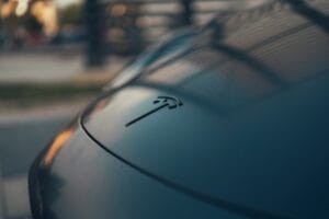 Close-up af Tesla-logo på en bil i skumringen, fremhæver det elegante design og Tesla's innovative teknologi