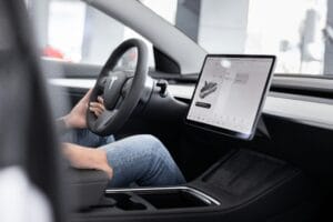 Person sidder i førersædet af en Tesla-bil med fokus på den store touchskærm på instrumentbrættet