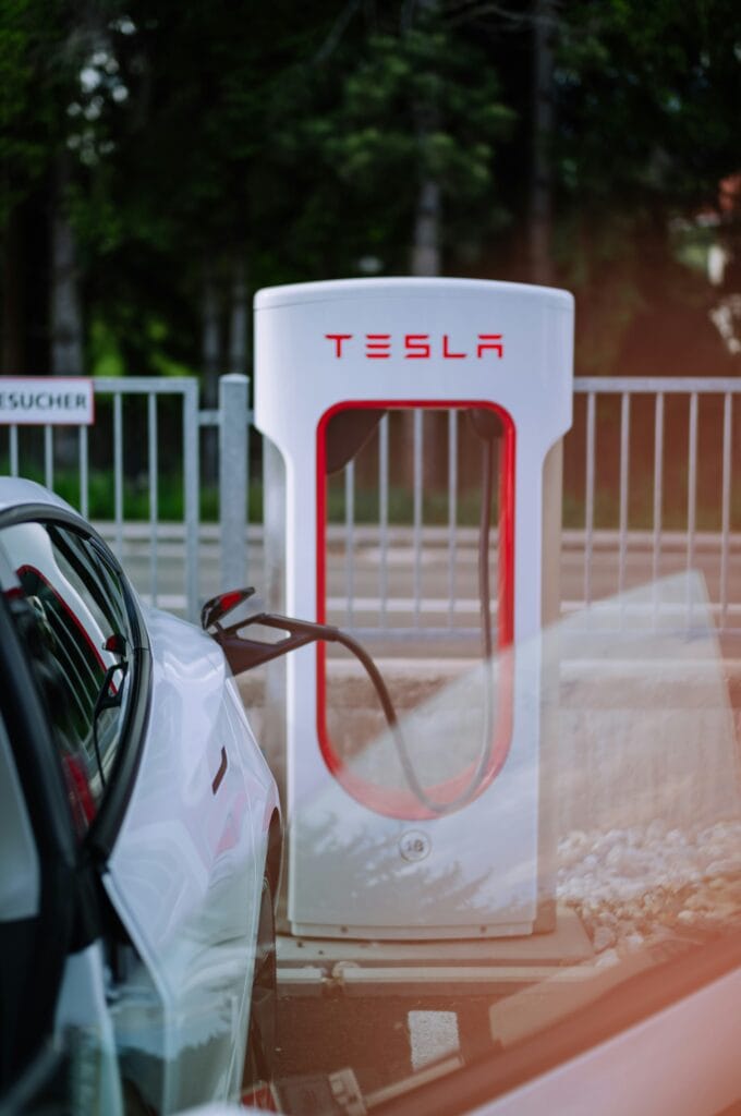 Hvid Tesla Model 3 oplader ved en Tesla Supercharger station ved en skovkant