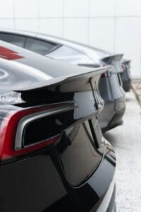 Nærbillede af bagenden på en sort Tesla med elegant spoiler, parkeret ved siden af andre Tesla-biler på en lys baggrund.