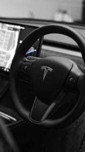 Sort Tesla-rat med mærkelogo og en digital skærm i baggrunden, der viser navigationsdata.