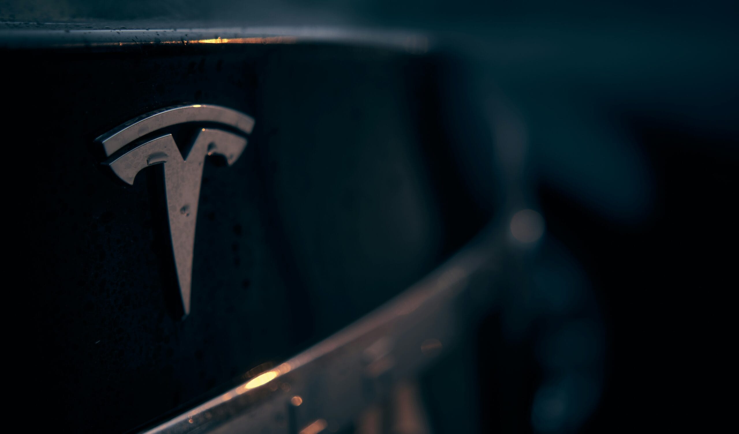 Close-up af Tesla-logo på en bil med mørk baggrundsbelysning