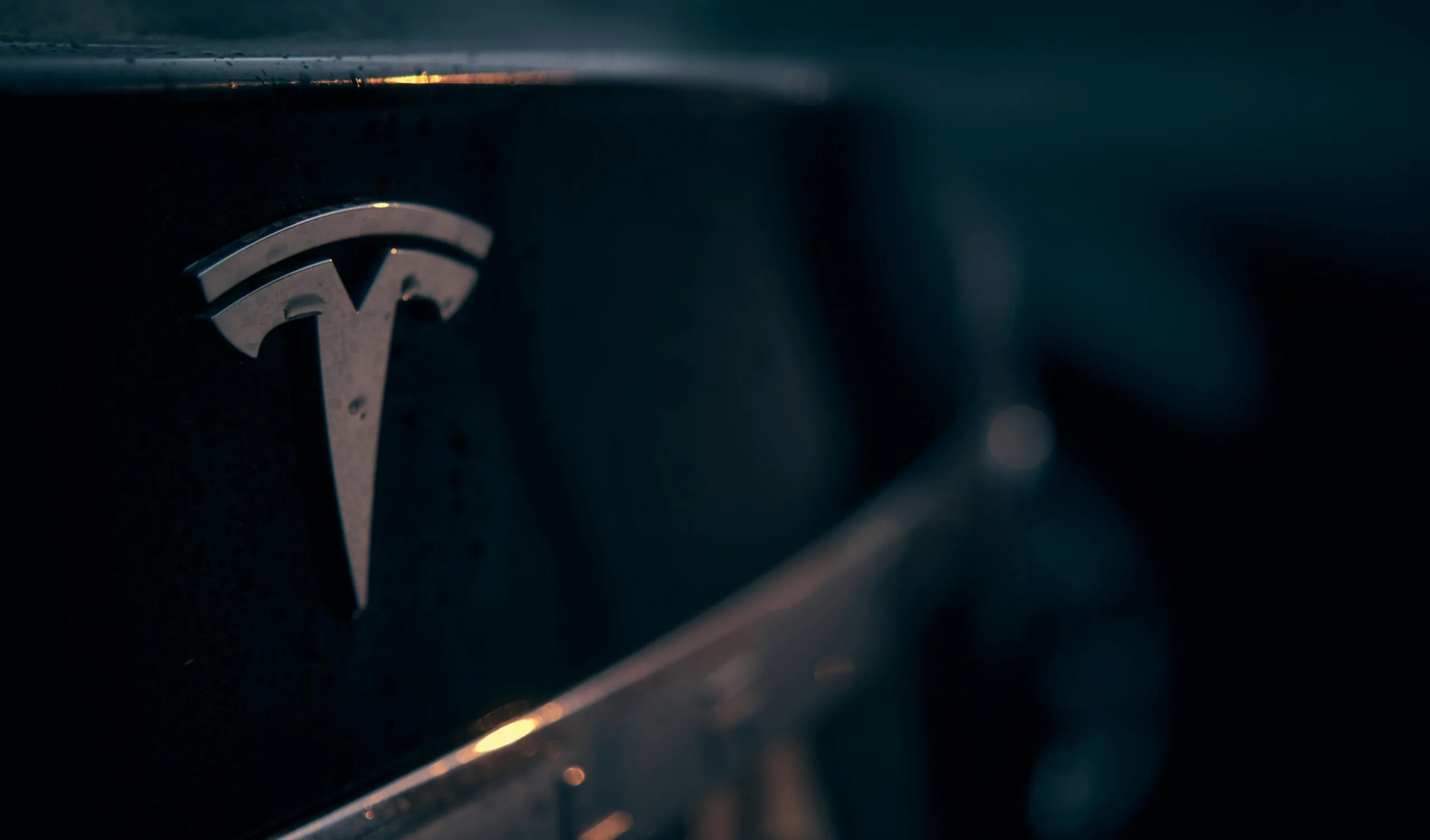 Close-up af Tesla-logo på en bil med mørk baggrundsbelysning