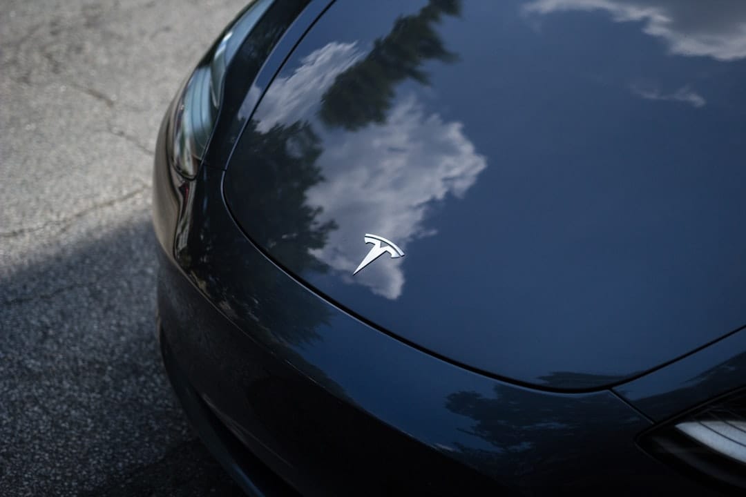 Tesla-logo på sort bilkofanger med refleksion af sky og træer