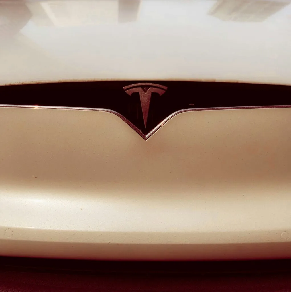 Tæt på Tesla-logo på forenden af en elbil med en skinnende perlehvid lakering.