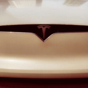 Tæt på Tesla-logo på forenden af en elbil med en skinnende perlehvid lakering.