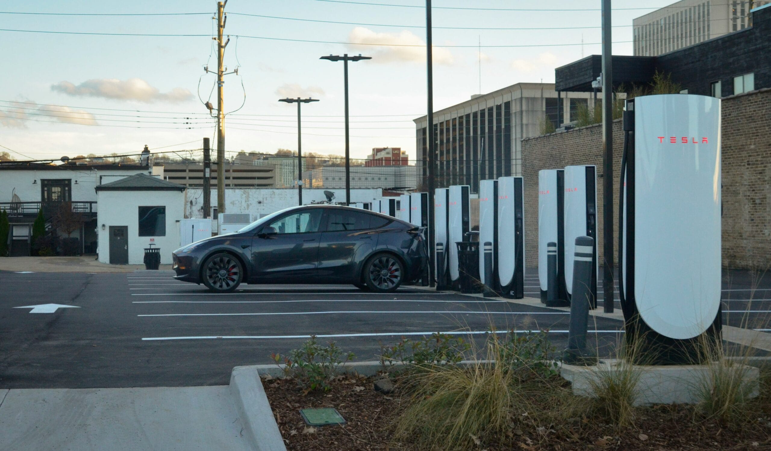 Tesla elbil oplader ved en række Tesla Supercharger-stationer på en parkeringsplads i en by.