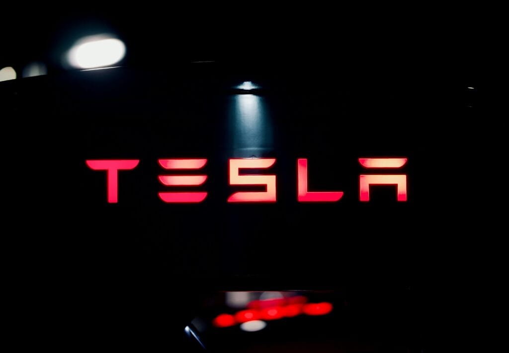 Tesla logo oplyst i rødt lys i mørkt miljø