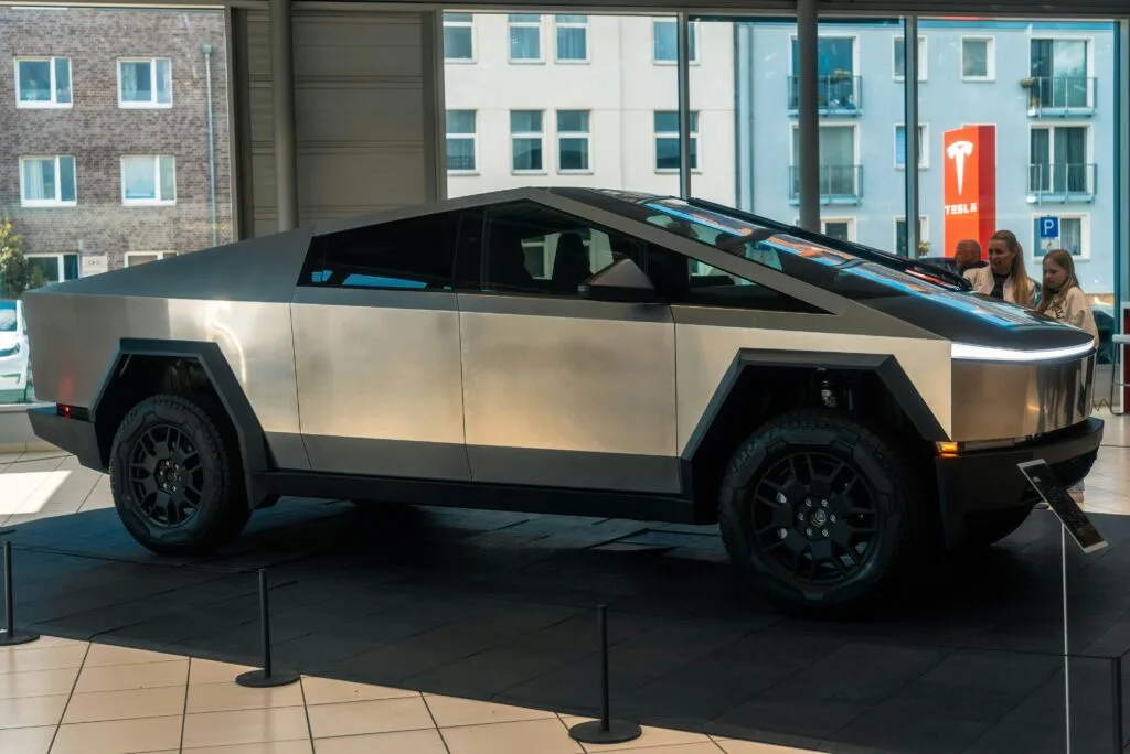 Tesla Cybertruck udstillet i et showroom med lysindfald fra store vinduer og baggrund af bybygninger.