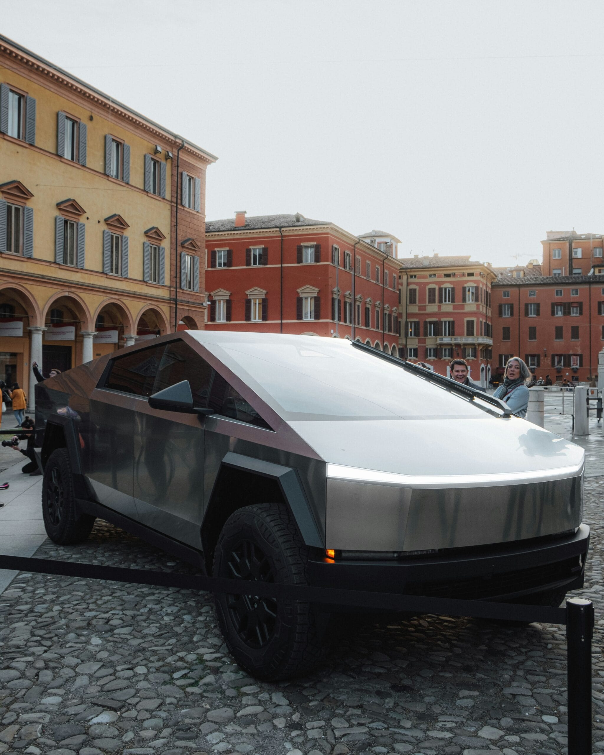 Tesla Cybertruck parkeret på brostensbelagt plads foran farverige europæiske bygninger.