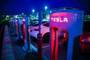 Tesla Supercharger-station oplyst i mørket med flere elbiler parkeret omkring.