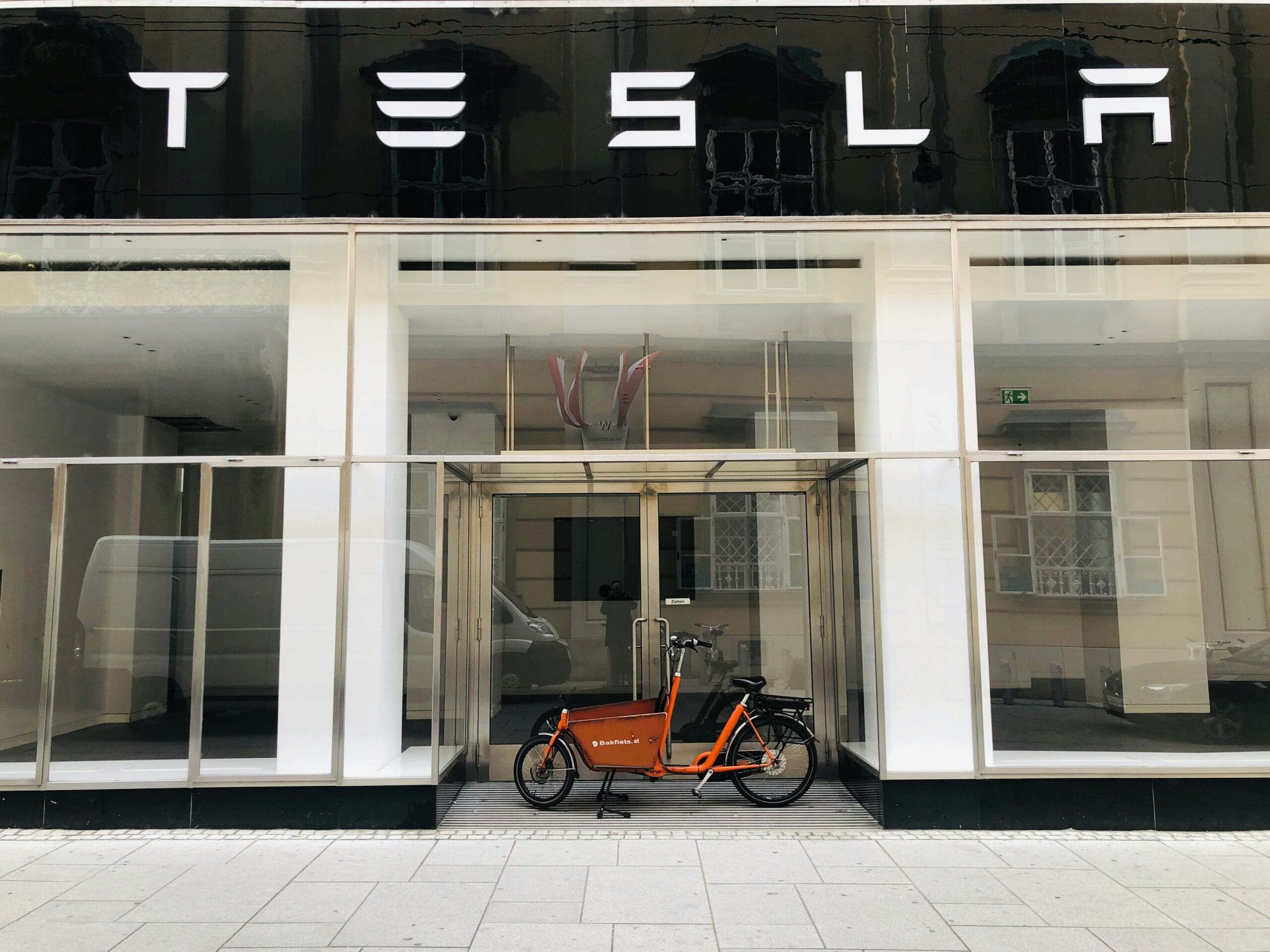Tesla butik med glasfacade og en orange ladcykel parkeret foran.