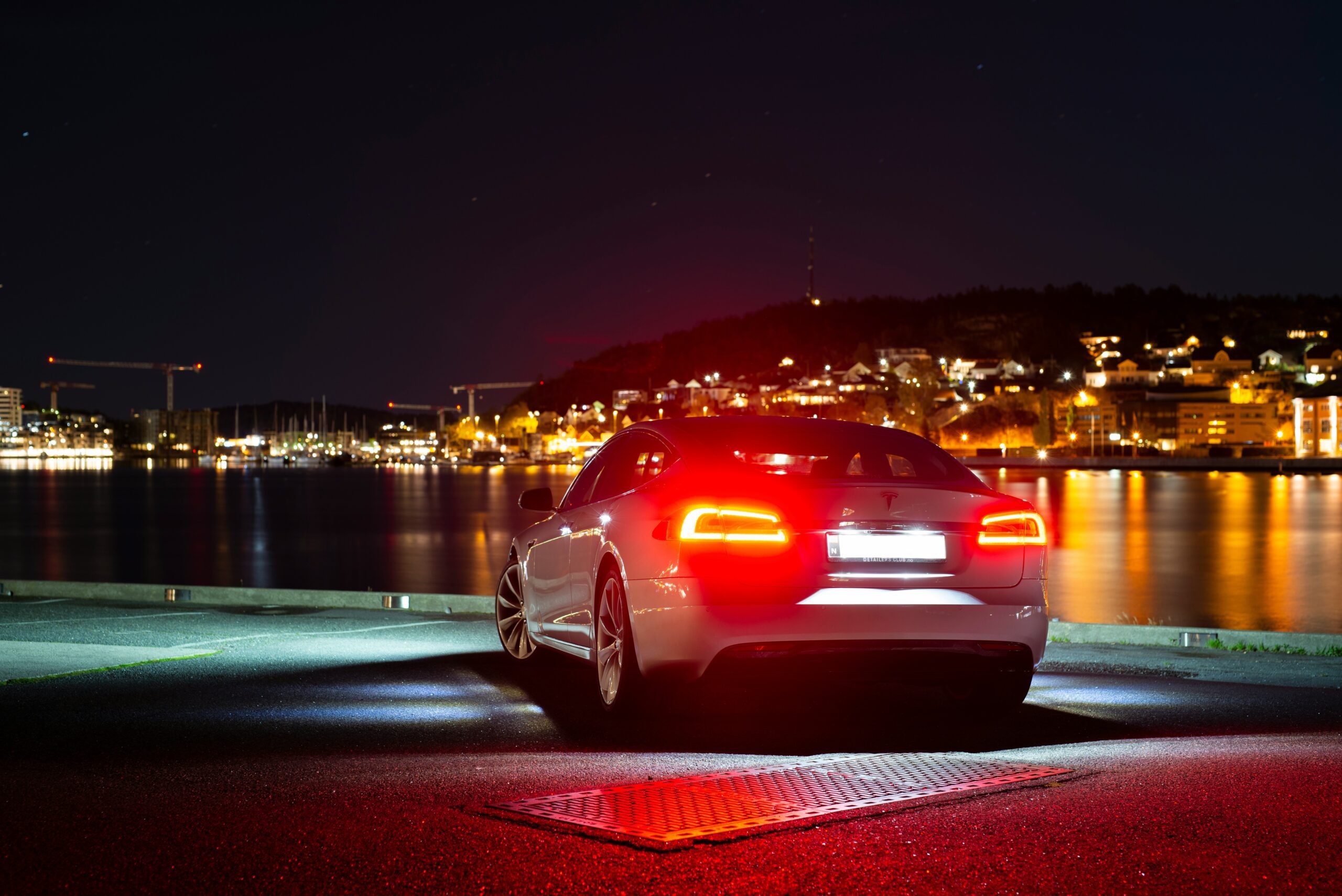 Tesla elbil ved havnen om natten med byens lys i baggrunden