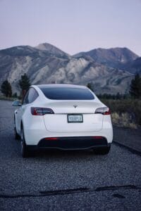 Hvid Tesla bil på åben vej foran bjerge i skumringen