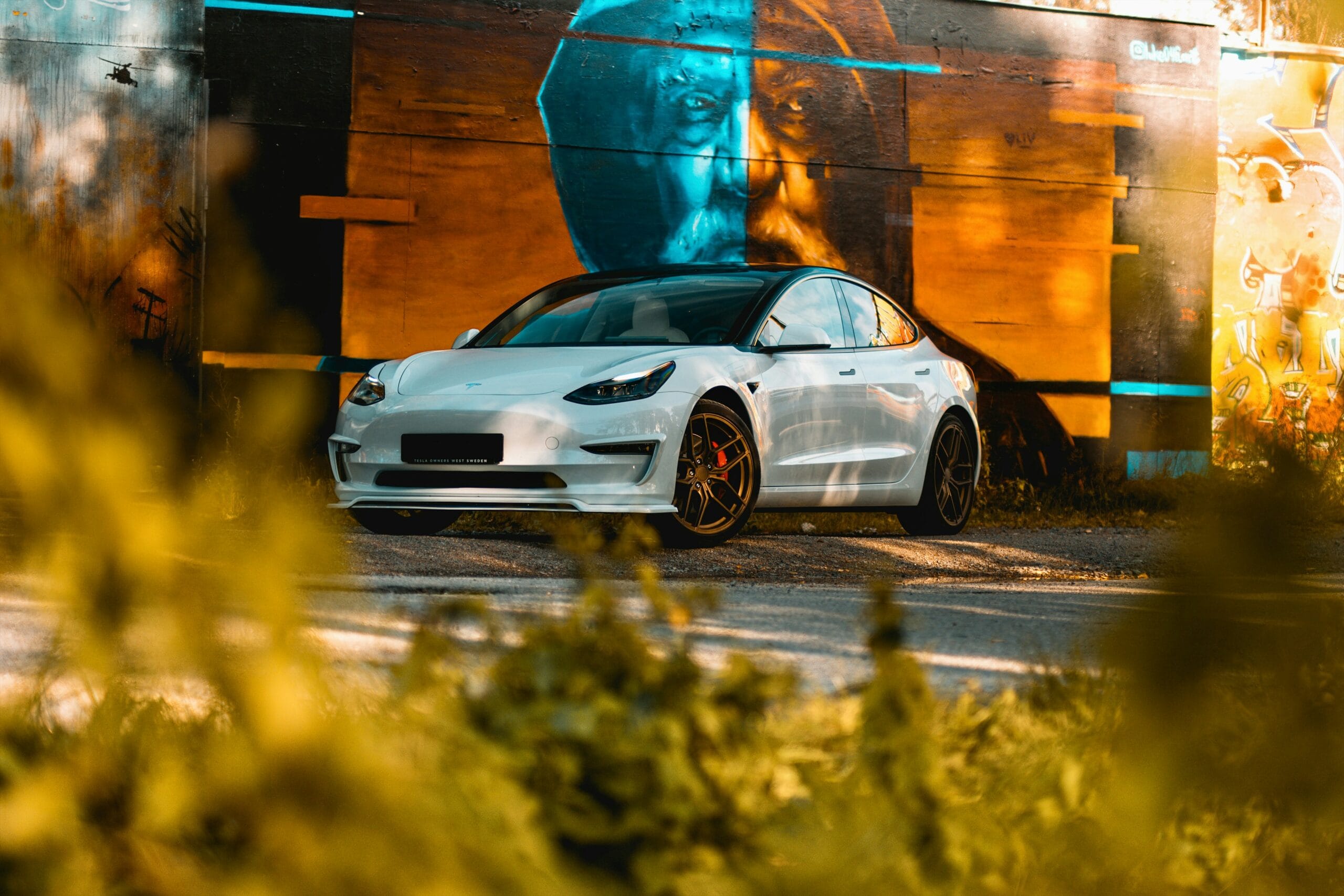 Hvid Tesla Model 3 foran farverig graffiti væg