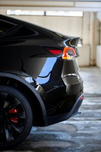 Bagside af en sort Tesla Model Y med skarpe linjer og røde bremsekalibre, parkeret i en garage.