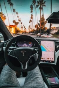 Interiør af en Tesla-bil med udsigt over palmeklædt gade ved solnedgang