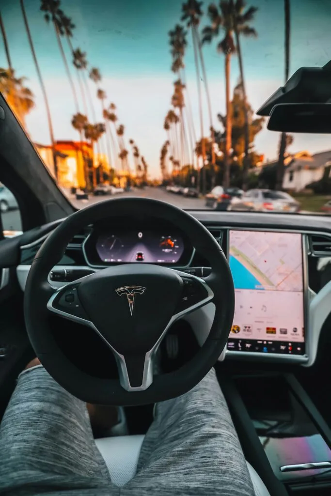 Interiør af en Tesla-bil med udsigt over palmeklædt gade ved solnedgang