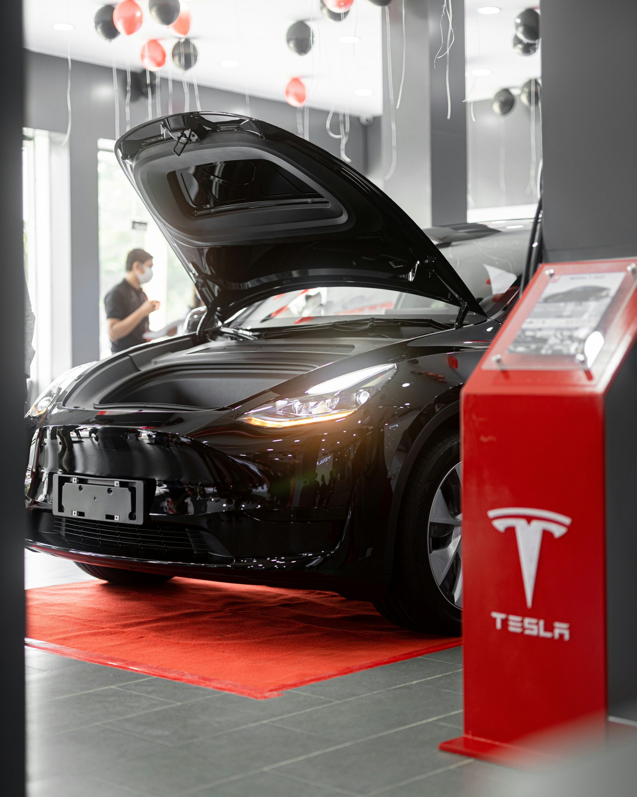 Sort Tesla med åbnet fronthjelm i showroom med røde og sorte balloner i loftet