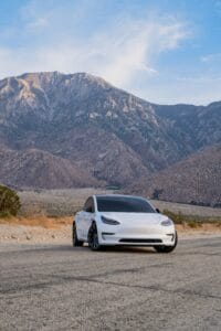 Hvid Tesla elbil med bjerge i baggrunden under en klar blå himmel