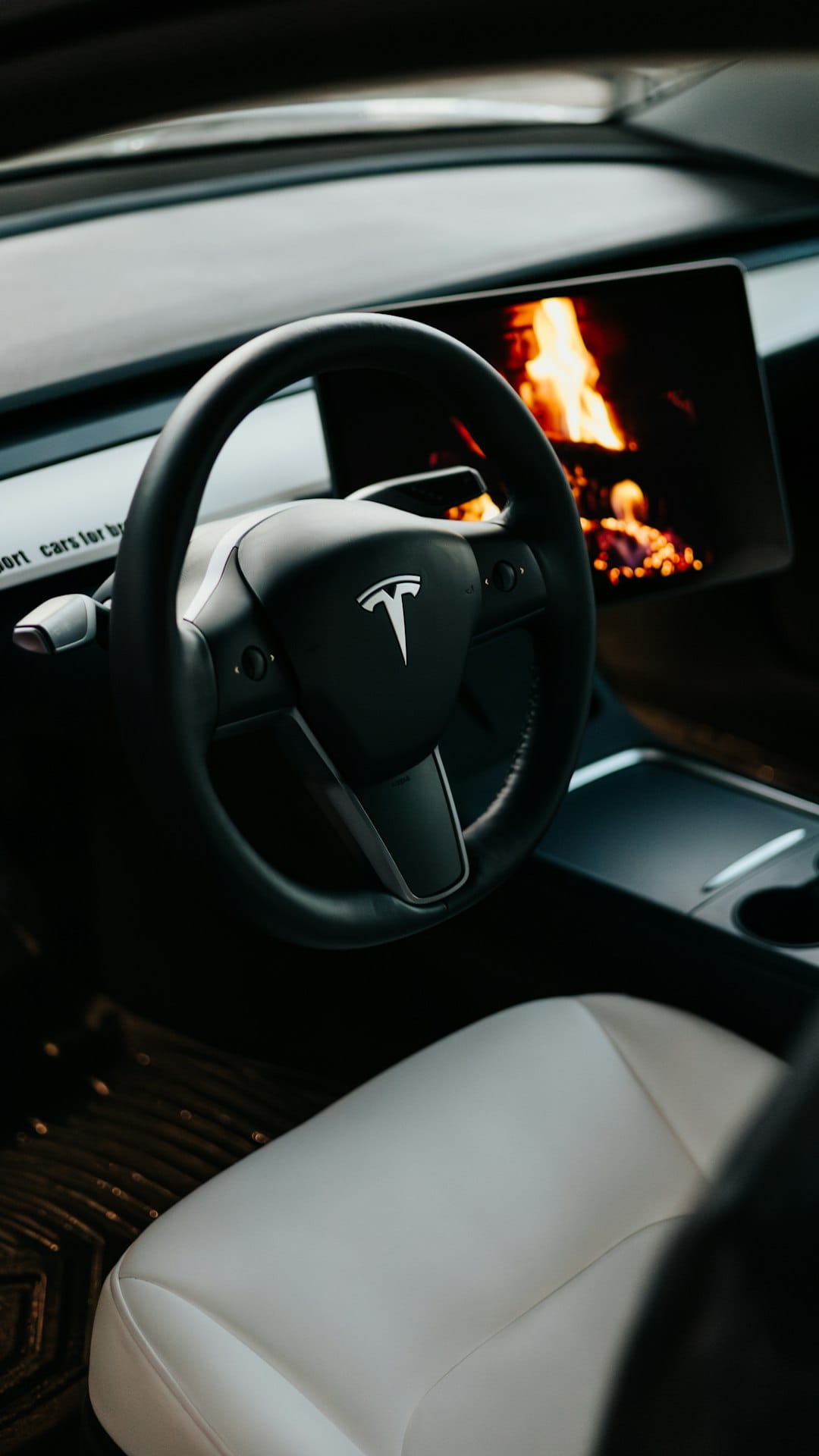 Tesla bilinteriør med minimalistik rat og moderne skærm, der viser pejs.