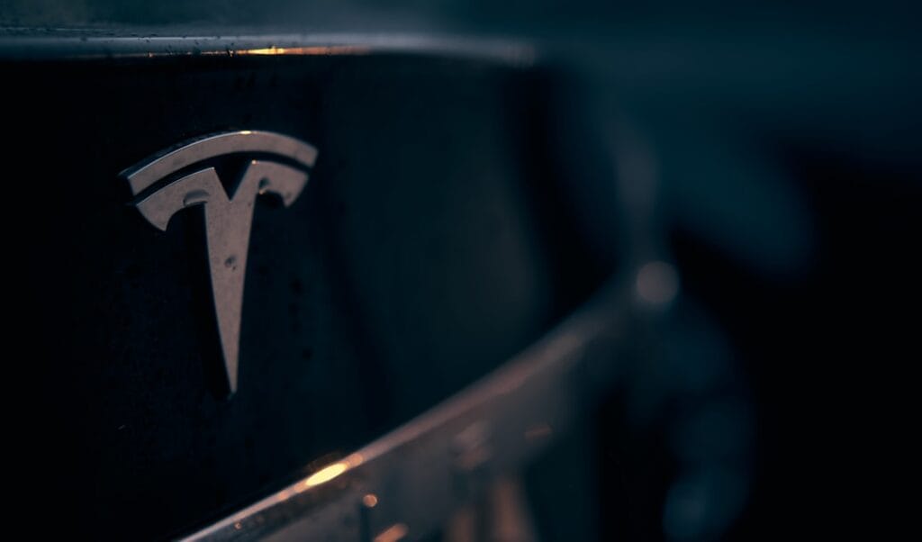 Tesla-logo set tæt på i lav belysning, symboliserende teknologisk innovation og moderne bilindustri