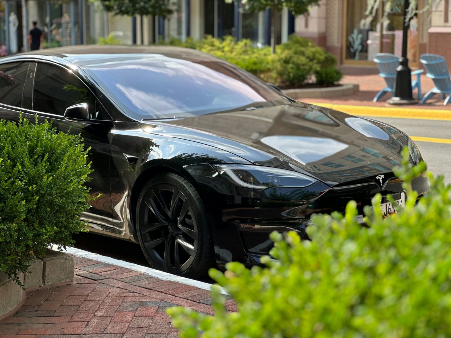 Sort Tesla Model S parkeret ved byens gade med grønne buske i forgrunden