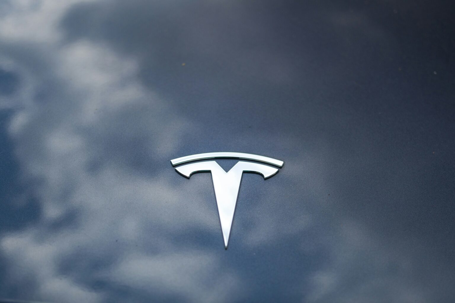 Tesla-logo på bilens kølerhjelm med en refleksion af himlen