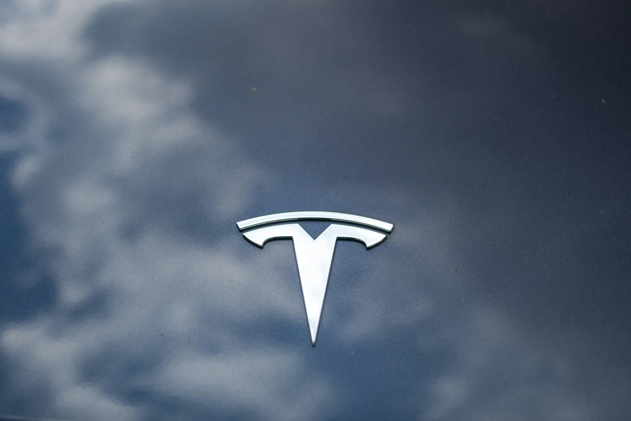 Tesla-logo på bilens kølerhjelm med en refleksion af himlen