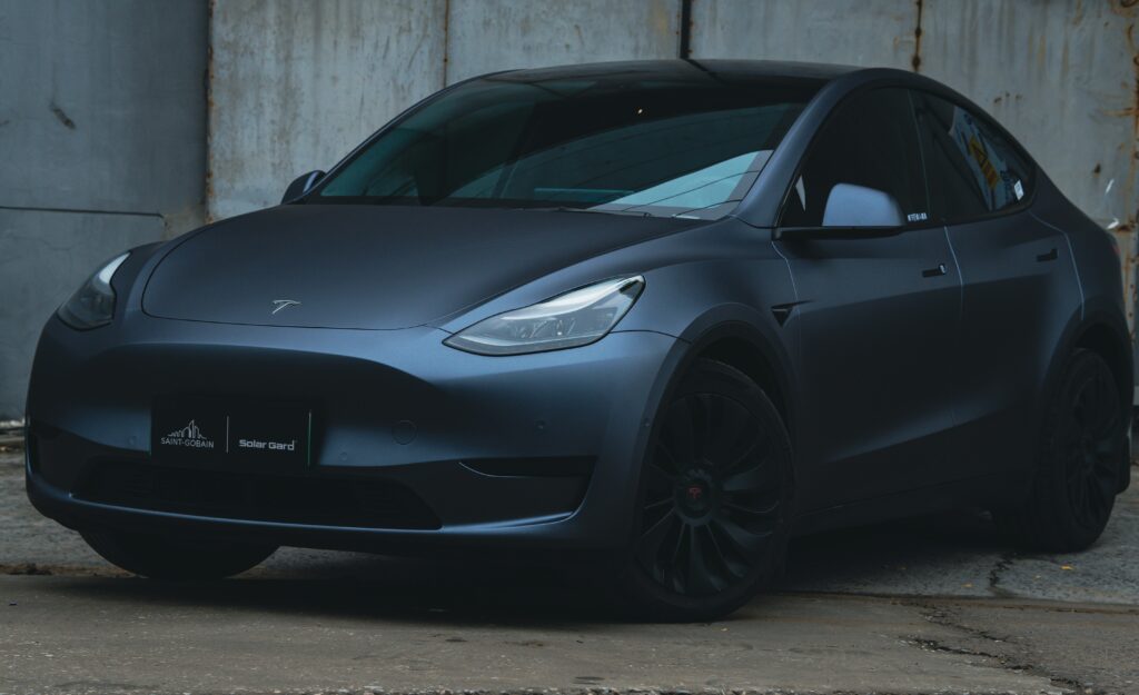 Matgrå Tesla Model Y parkeret foran en industriel baggrund