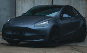Matgrå Tesla Model Y parkeret foran en industriel baggrund