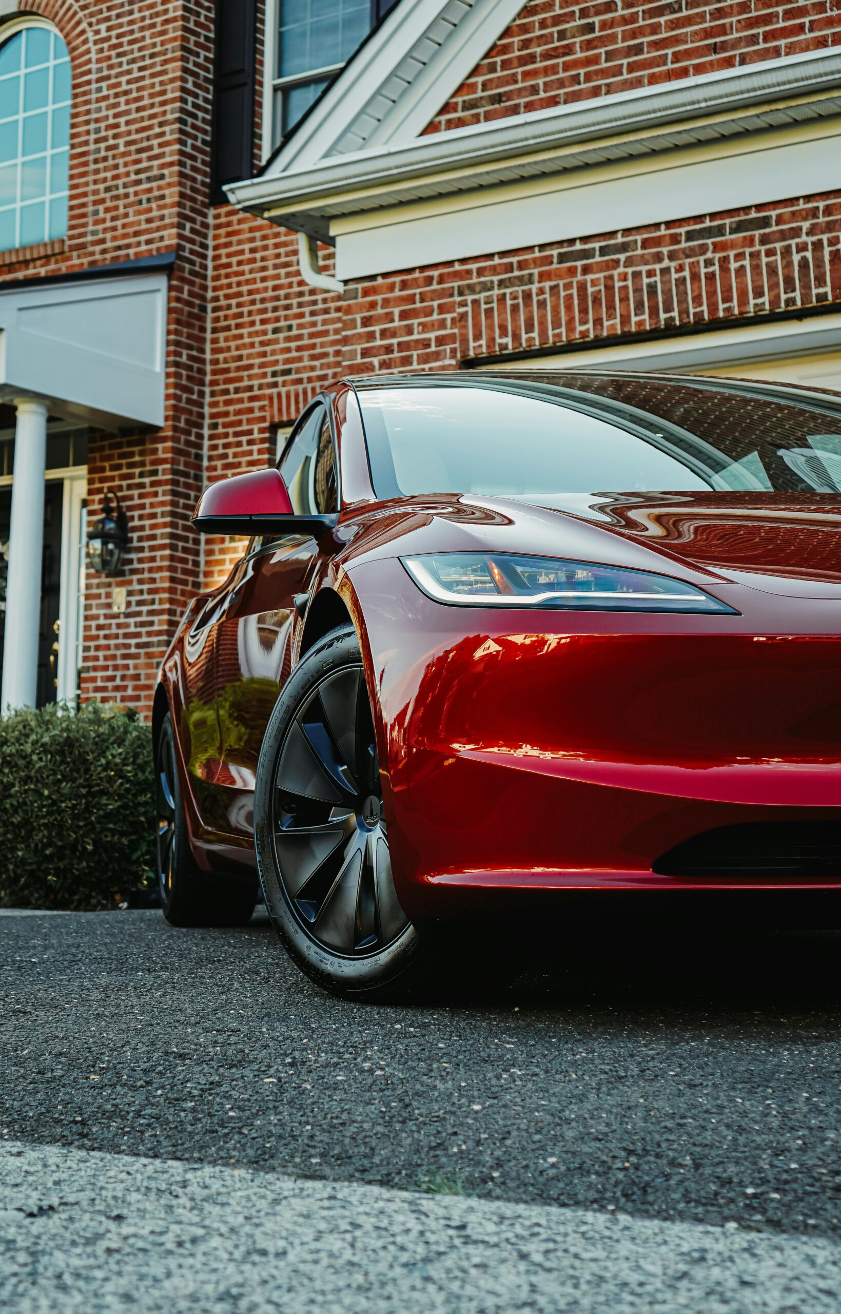 Rød Tesla foran et murstenshus, fremhæver bilens elegante design og moderne teknologi.
