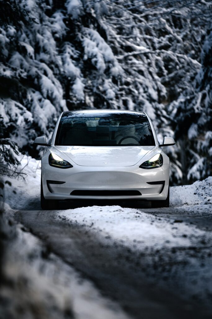 Tesla Model 3 kører gennem snedækket skovvej om vinteren