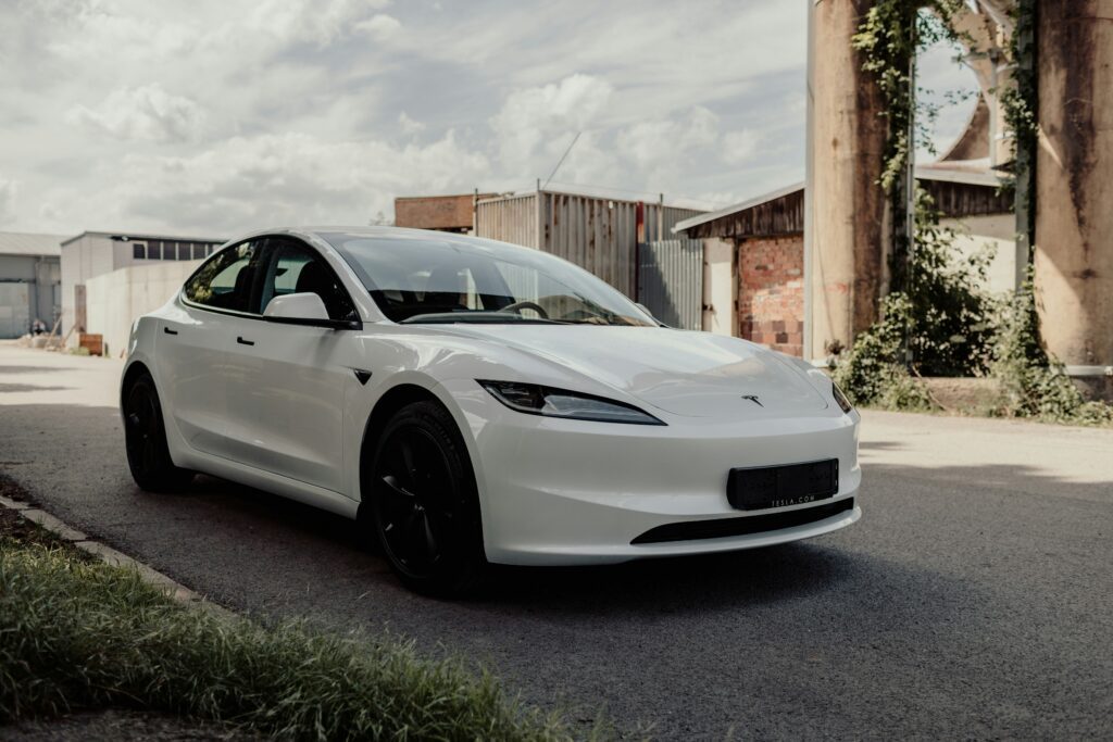 Hvid Tesla elbil parkeret foran industribygninger