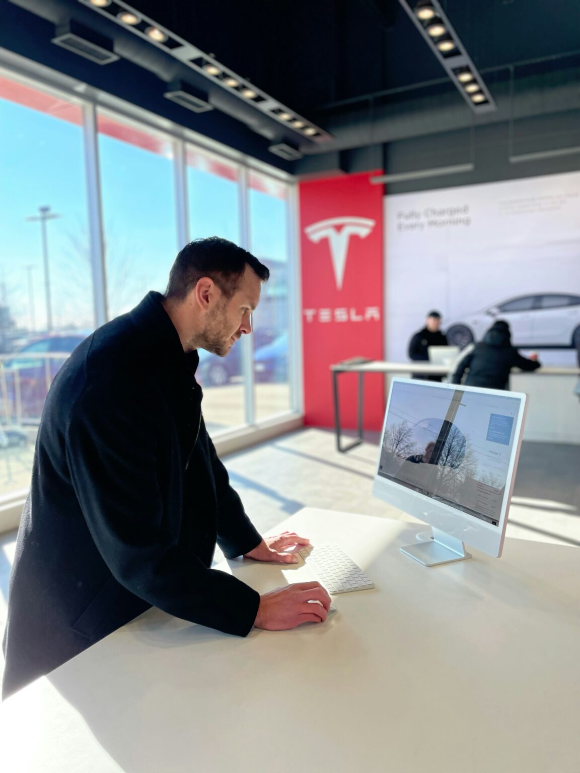 Mand ved computer i Tesla butik med elbil i baggrunden