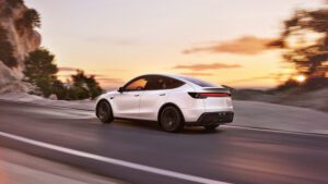 Hvid Tesla kører ned ad naturskøn vej ved solnedgang