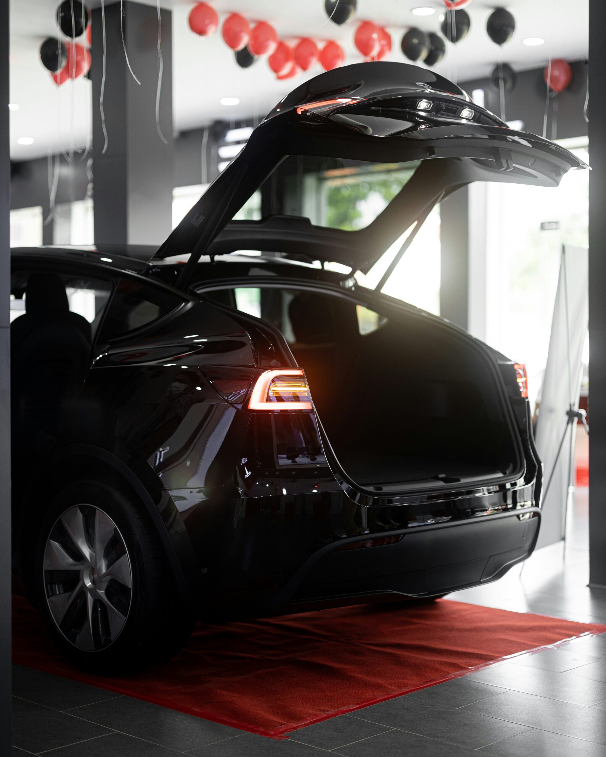 Bagenden af en sort elektrisk bil med bagagerummet åbent, omgivet af røde og sorte balloner indendørs.