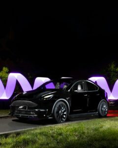 Sort Tesla elbil med futuristisk lyskunst i baggrunden om natten