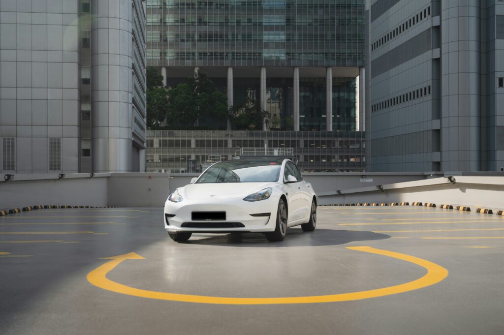 Hvid Tesla Model 3 parkeret i et moderne bymiljø med højhuse i baggrunden