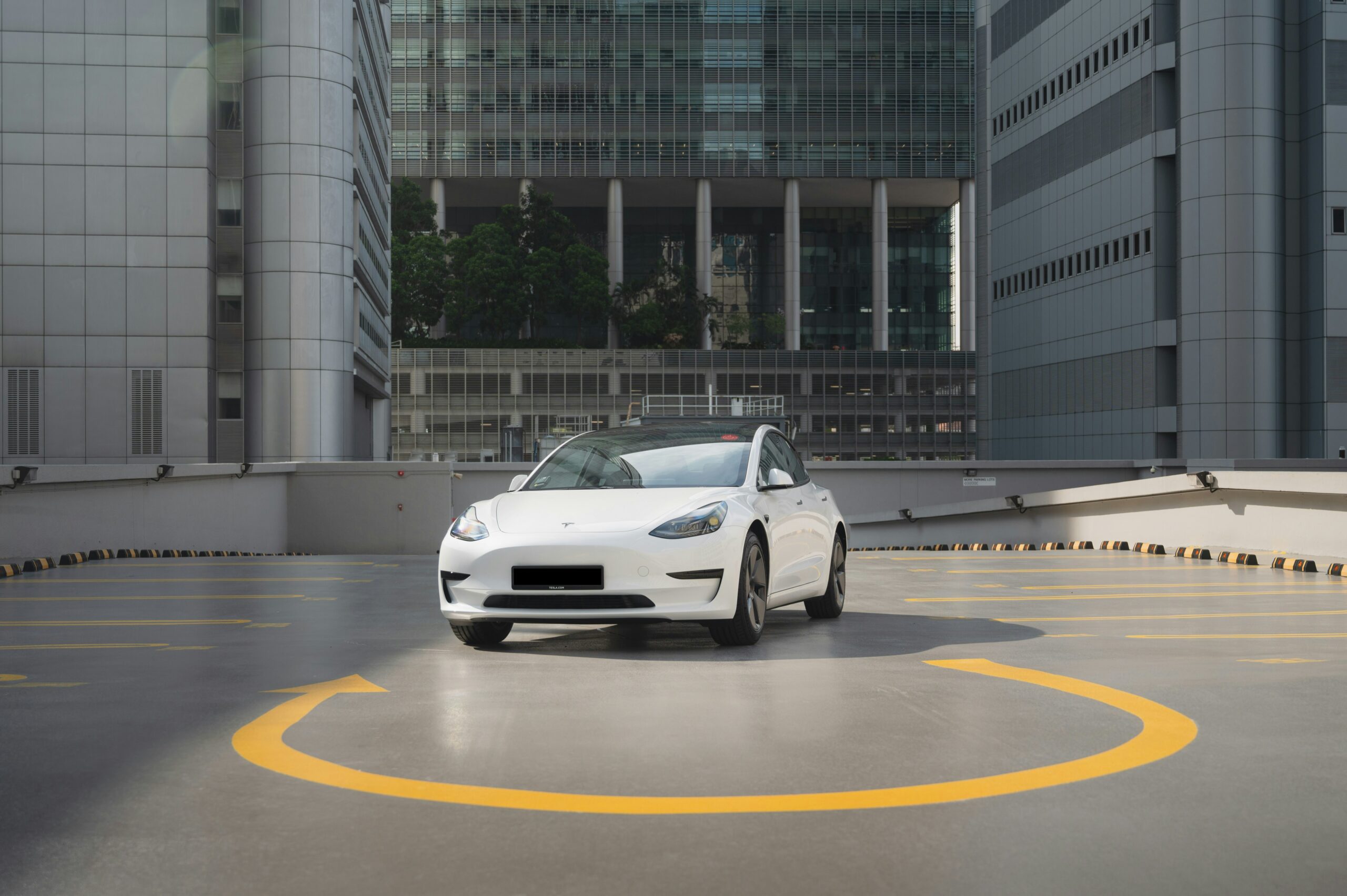Hvid Tesla Model 3 parkeret i et moderne bymiljø med højhuse i baggrunden