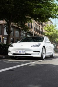 Hvid Tesla Model 3 parkeret på gaden under træer i bymiljø