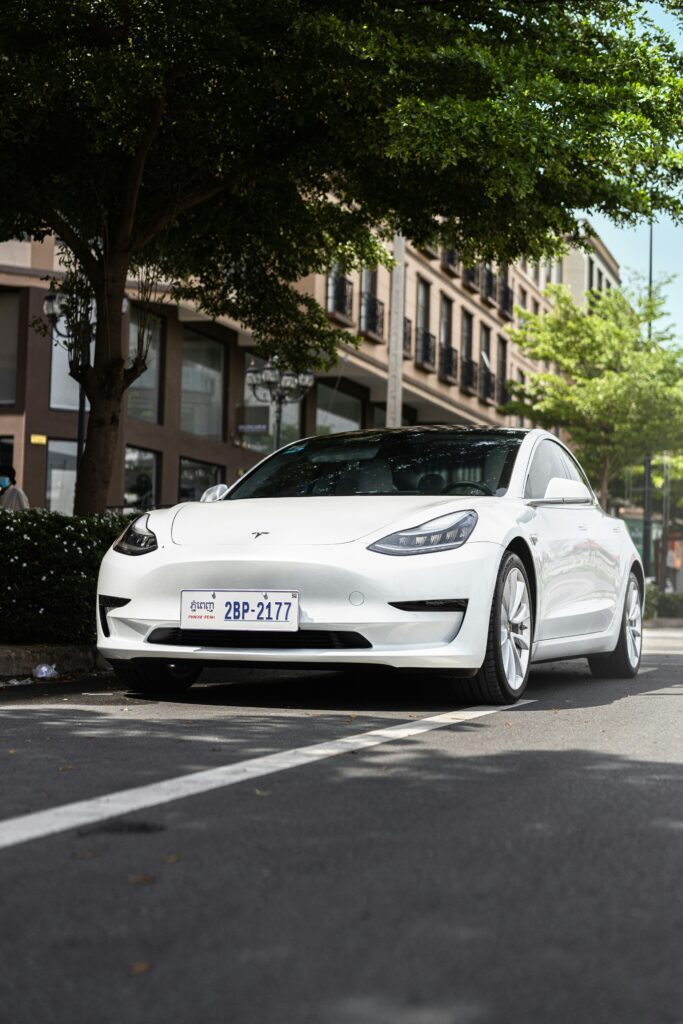 Hvid Tesla Model 3 parkeret på gaden under træer i bymiljø