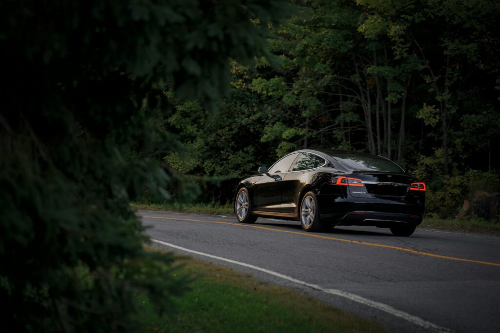 Sort Tesla Model S kører gennem en skovklædt vej