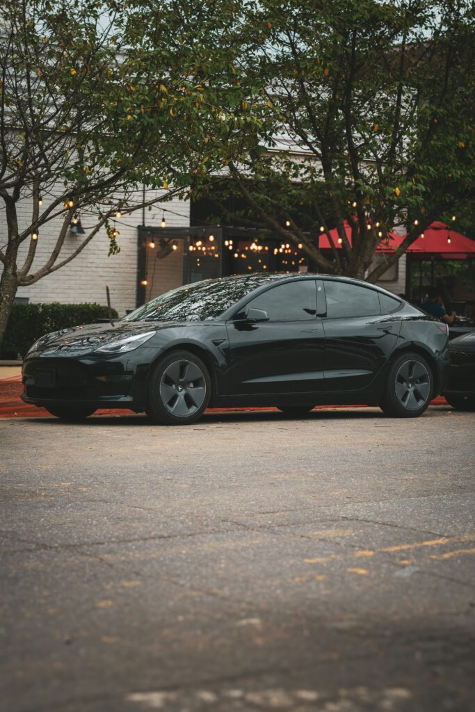 Sorte Tesla parkeret foran en hyggelig café med lyskæder