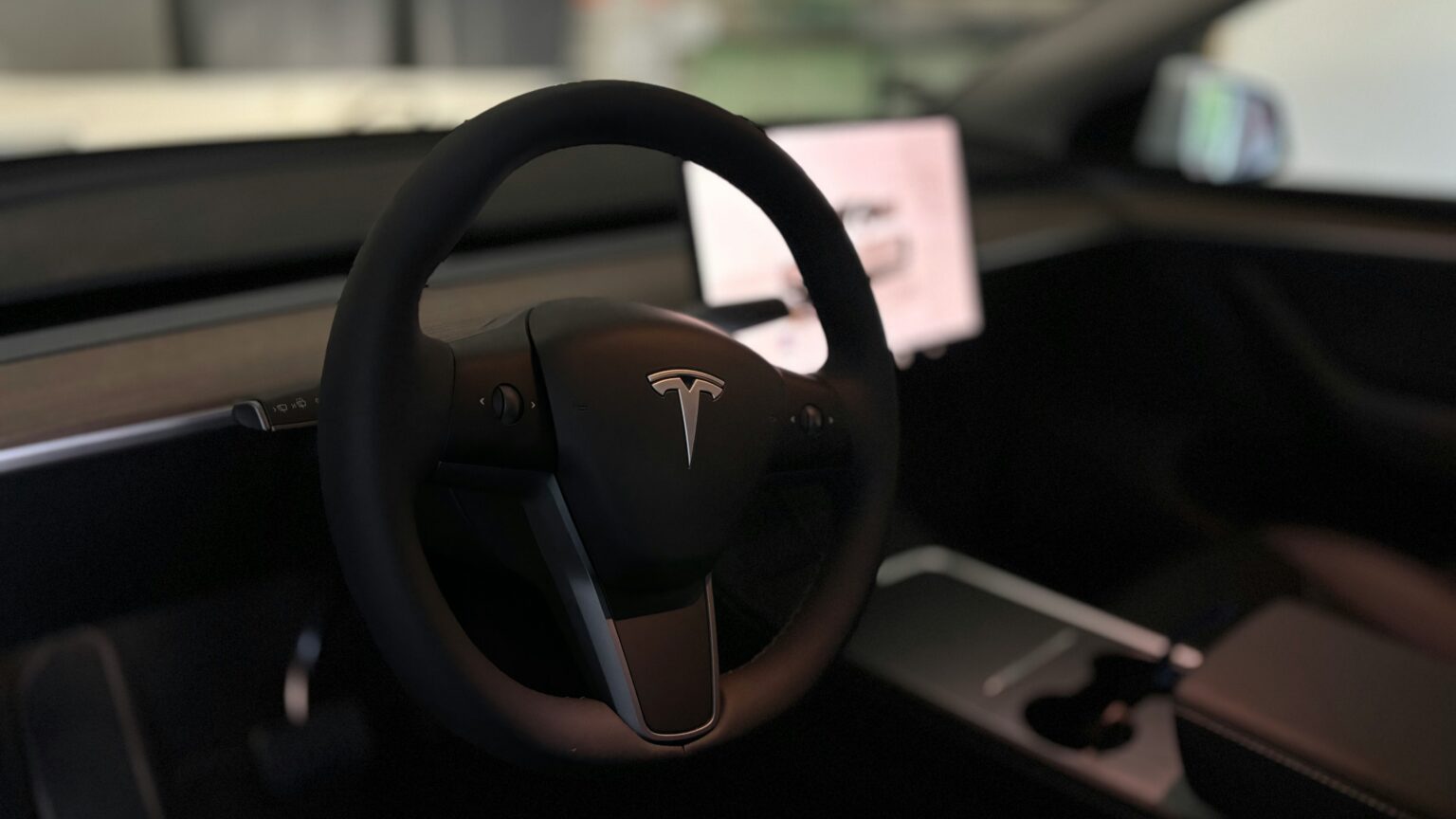 Rattet i en Tesla med minimalistisk interiør og central touchskærm.