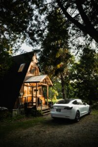 Hvid Tesla parkeret foran en træhytte i skoven