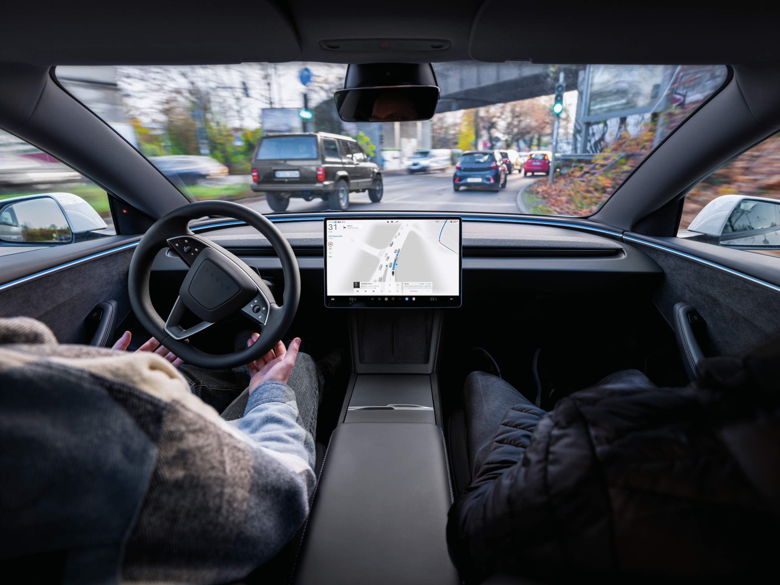 Indvendigt billede af en Tesla-bil på autopilot, hvor førerens hænder er frie fra rattet, med navigationsskærmen i fokus.